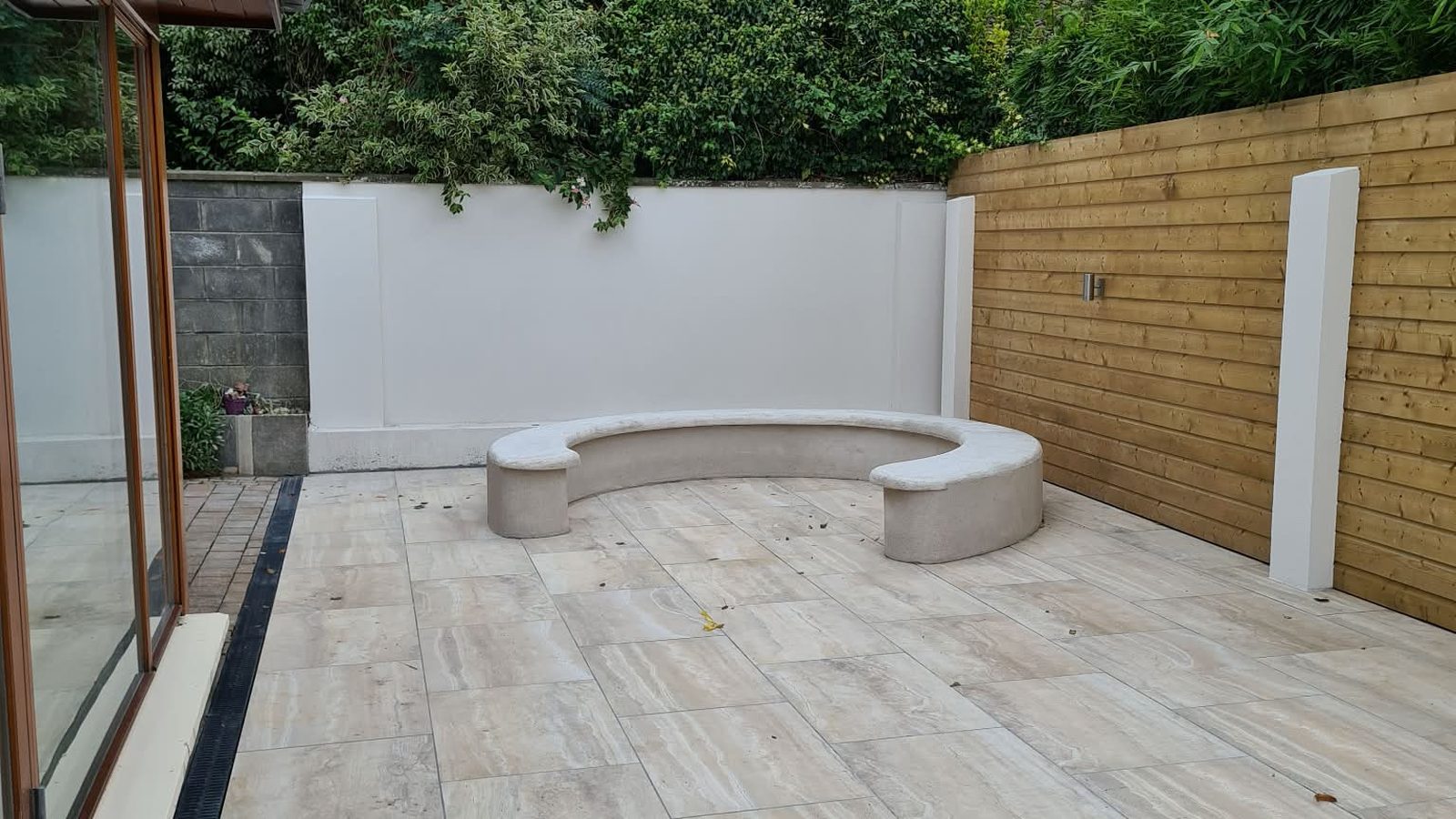 A finished patio with a curved seat, porcelain paving and a timber screen wall