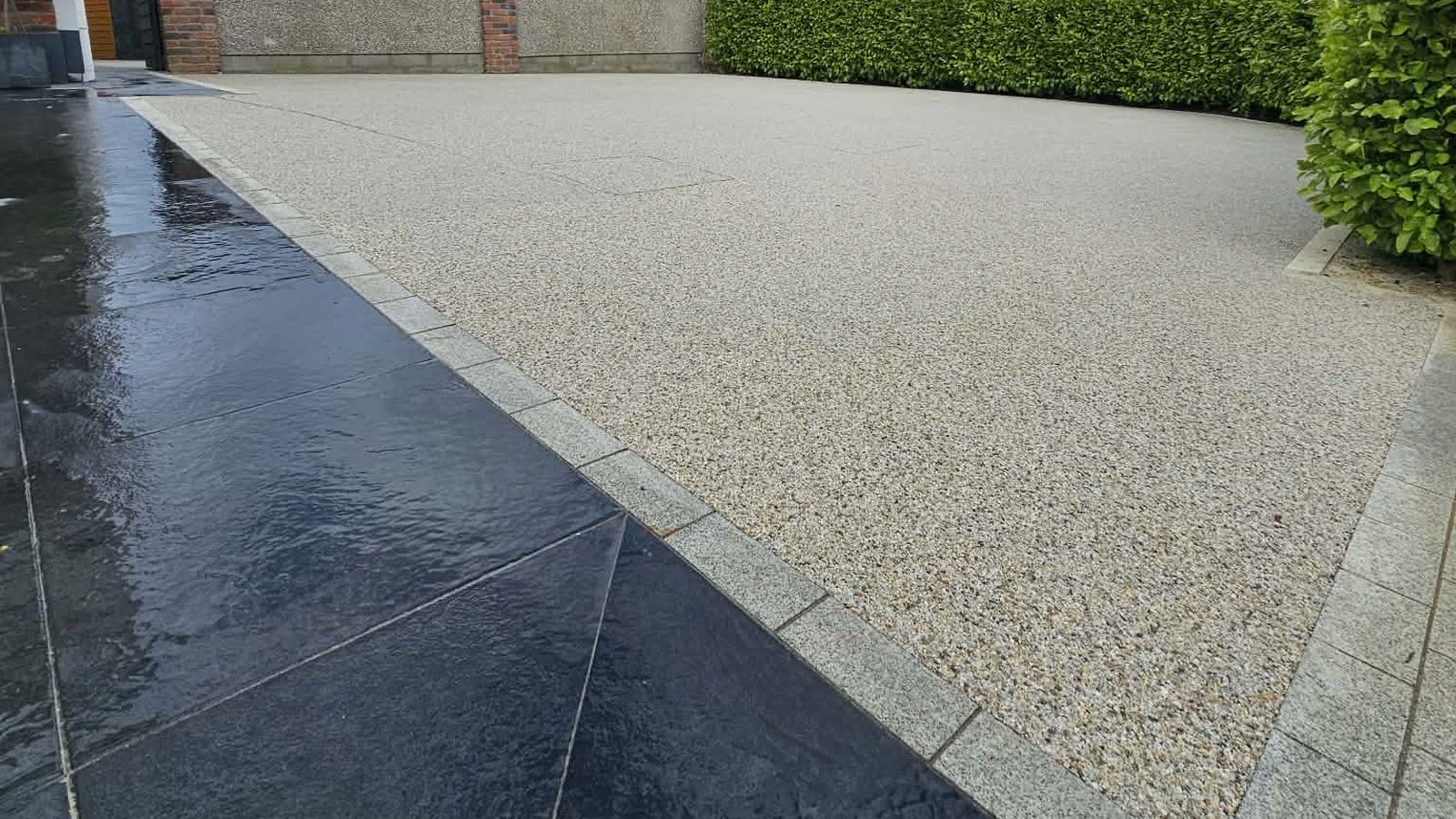 A finished resin bound driveway meeting dark granite paving along a granite sett edge