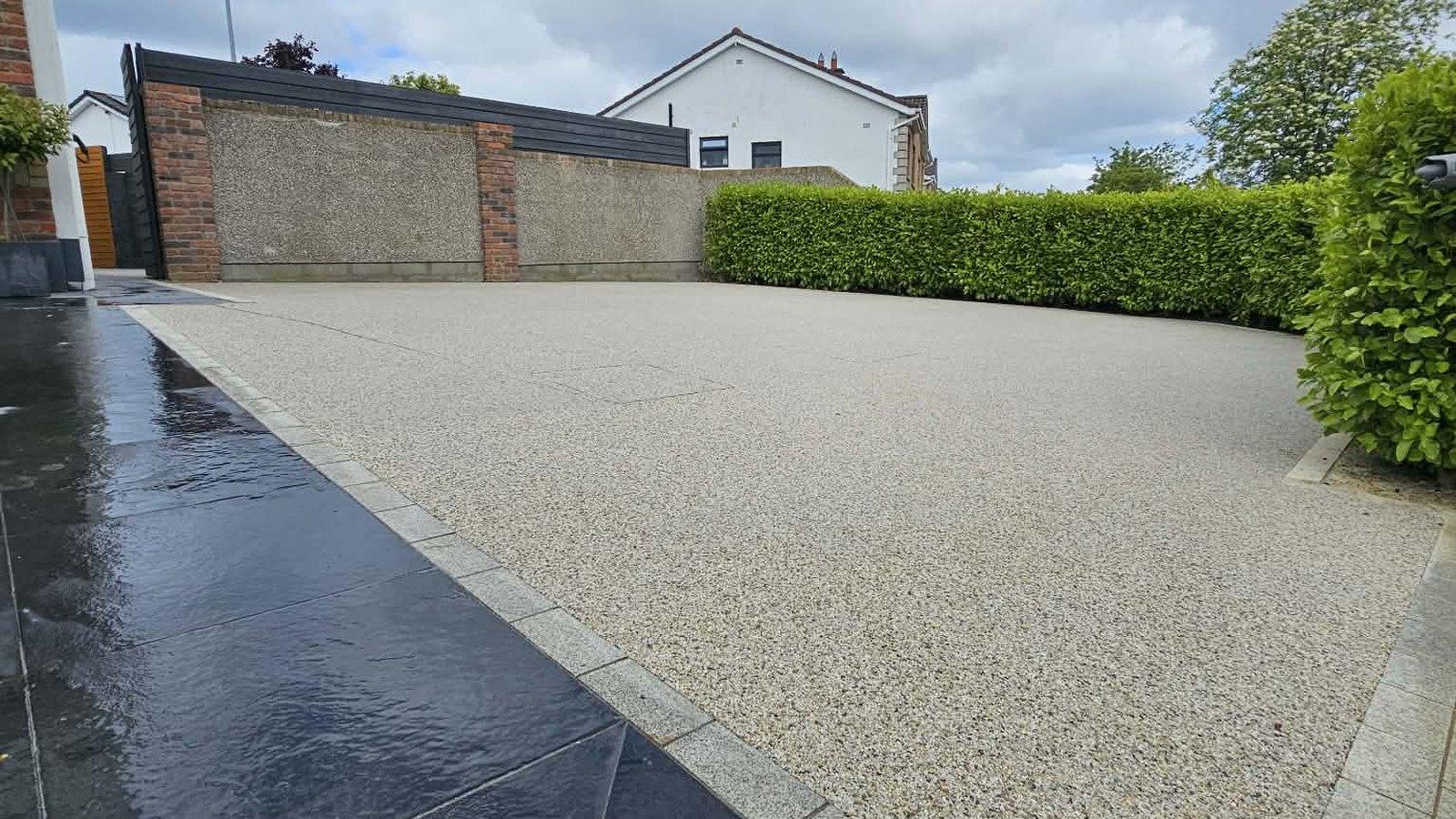 A finished resin bound driveway with a granite sett border, dark granite paving and a clipped hedge